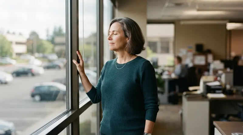 A woman taking a short break at a window with a view of a parking lot, chewing, eyes closed
