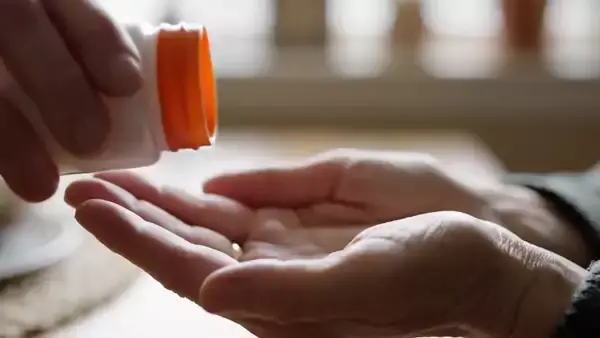 Two orange soft chews tipping from a small white jar into an open palm, seamless loop